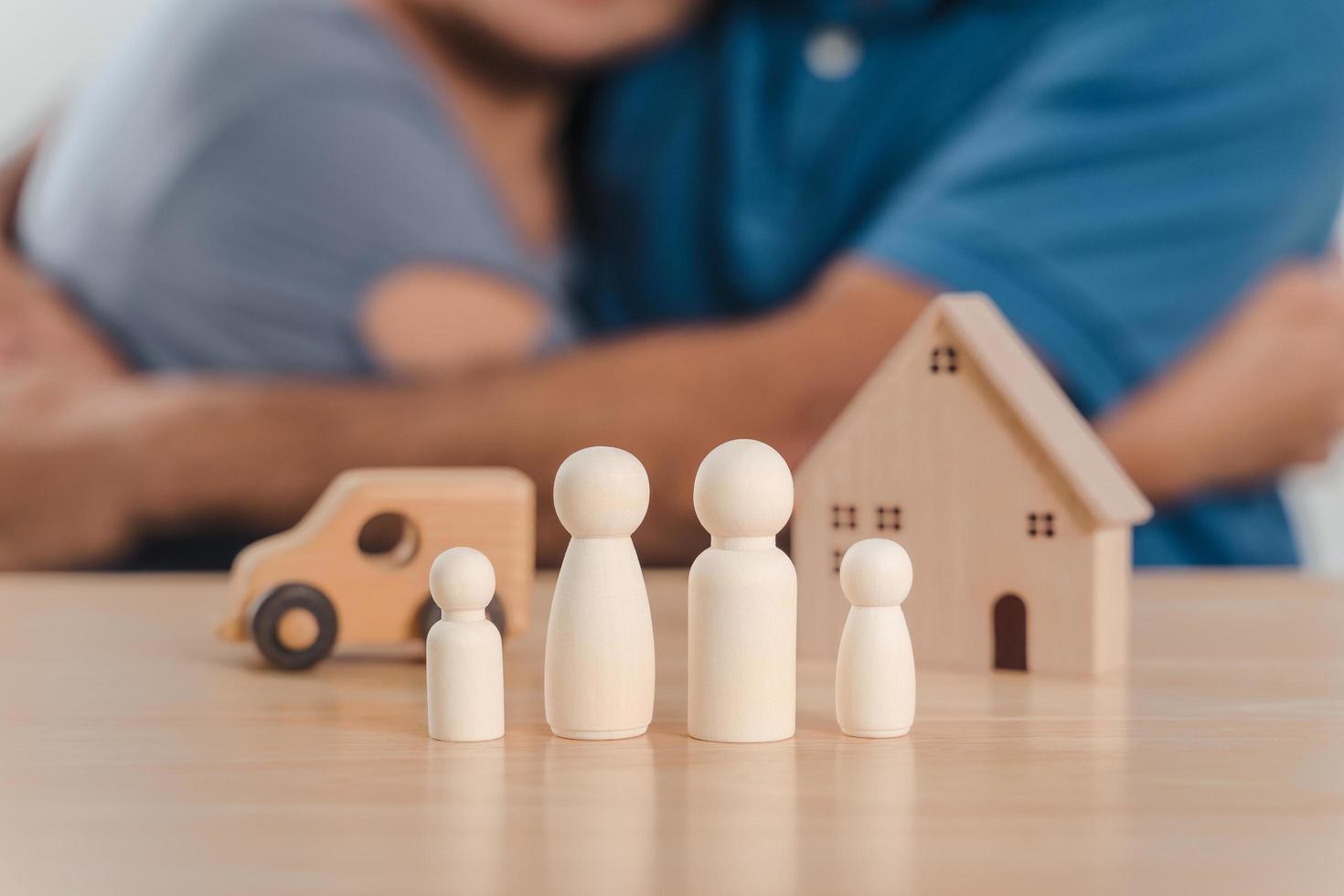 muñecas de clavijas de madera, casa de madera y auto con una pareja de hombres y mujeres abrazados. planificación, salvar a la familia, atención médica y seguros, salud mental familiar, día internacional de las familias foto