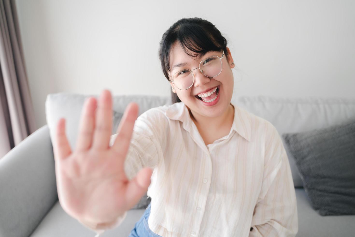 Young Asian woman using smartphone for online video conference call with friends waving hand making hello gesture photo