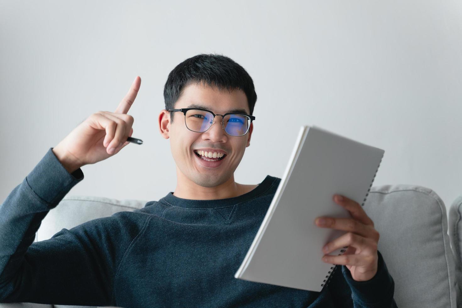 Young thoughtful Asian man in glasses thinking and looking at notebook. photo