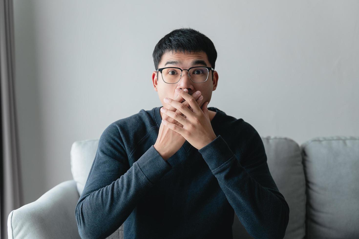 young man with shocked facial expression sitting on the sofa. photo