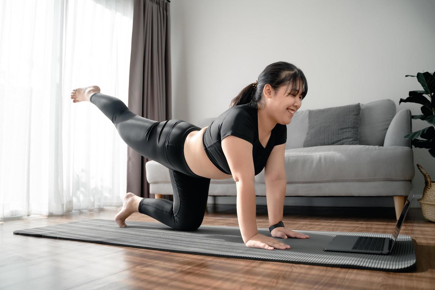 Asian chubby woman sitting on the floor in living room practice online yoga lesson with the computer. female having meditate training class on the laptop. photo