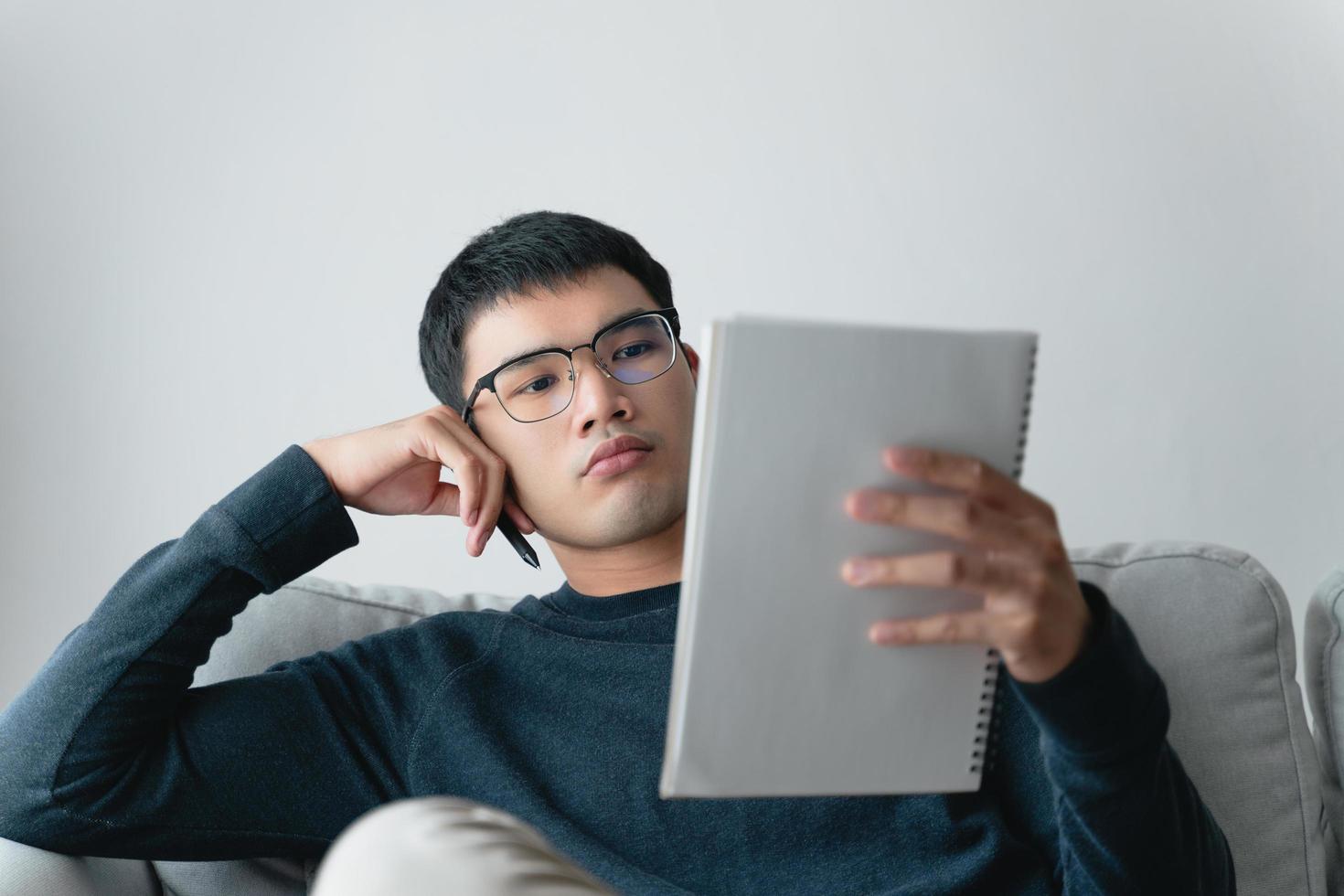 Young thoughtful Asian man in glasses thinking and looking at notebook. photo