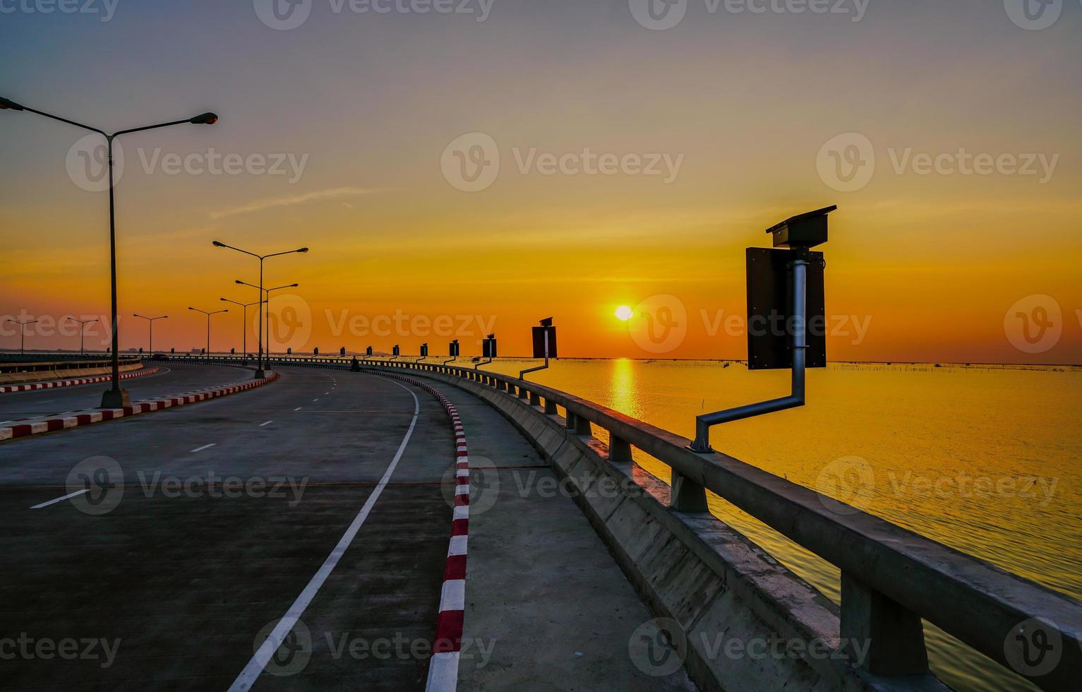 Curved coastal road with street lamp and orange sky at sunset in Chonburi, Thailand. photo