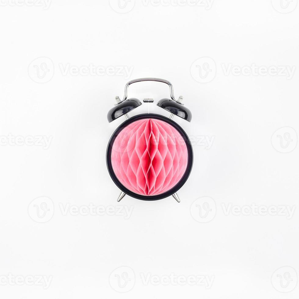 Black alarm clock with pink paper ball concept photo