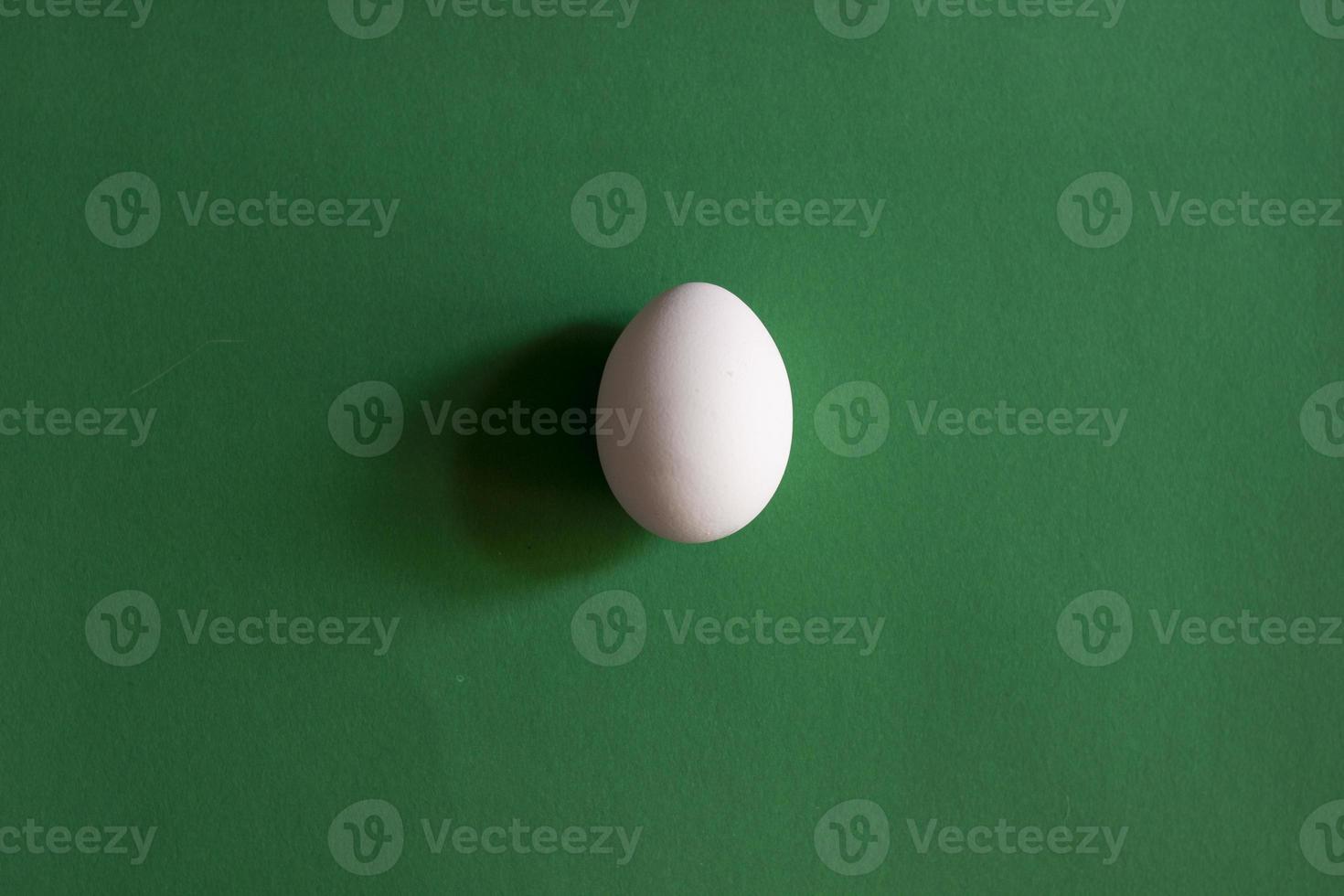 White chicken egg with shadow on green background, horizontal photo. Nature farm product, healthy food, single design element. Top view, object in center photo