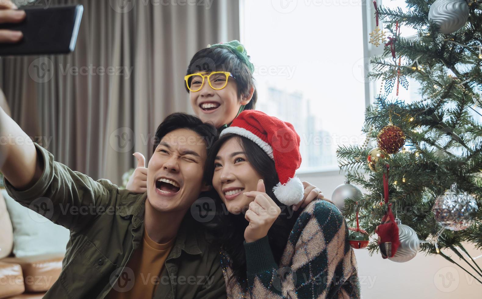 familia asiática tomando selfie cerca del árbol de navidad juntos en casa. familia, vacaciones, concepto de navidad foto