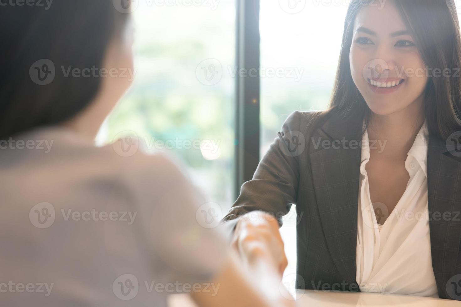 retrato joven mujer asiática entrevistadora y entrevistada dándose la mano para una entrevista de trabajo. gente de negocios apretón de manos en la oficina moderna. concepto de trato de saludo foto