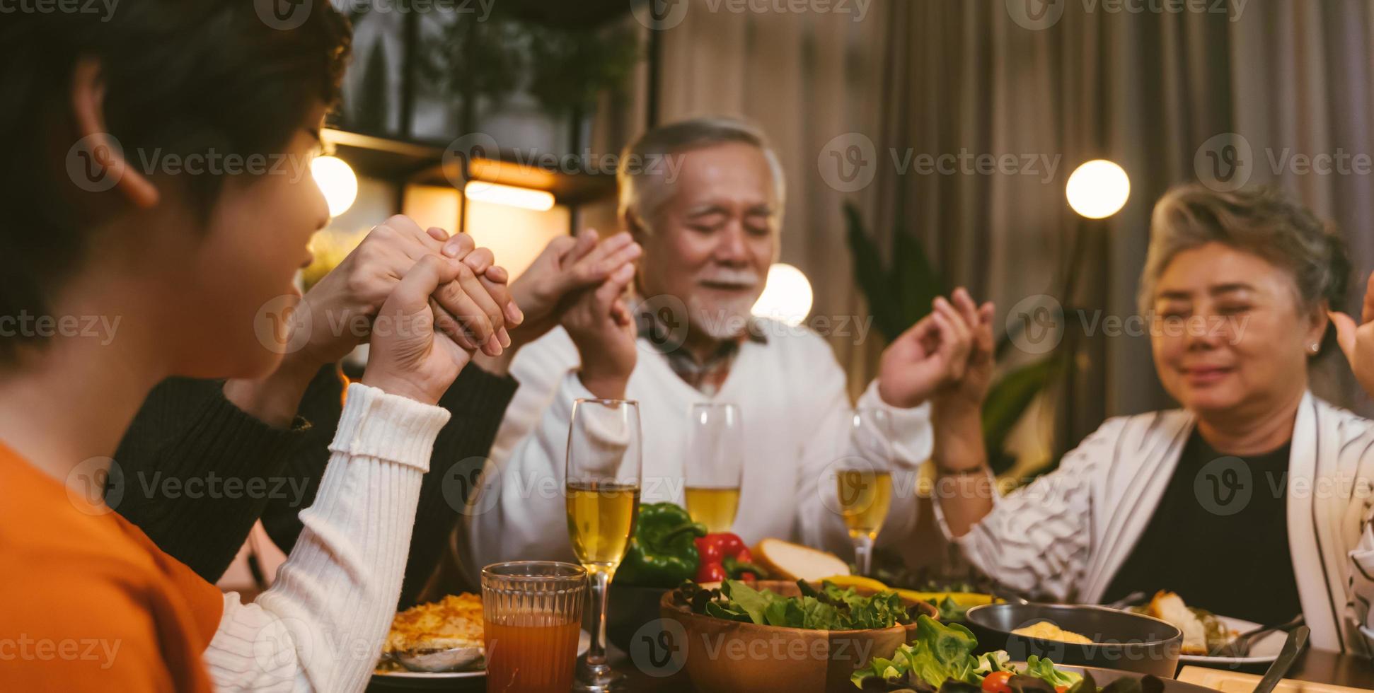 gran familia asiática cerrando los ojos al decir gracia orando antes de cenar en casa foto