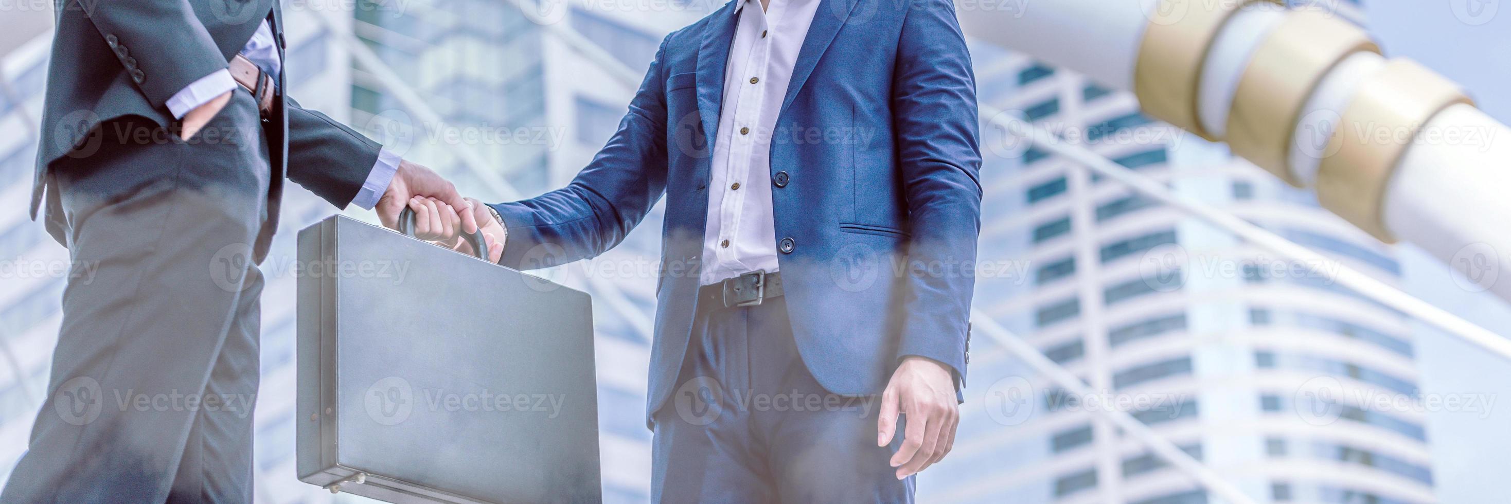 Businessman transfer deal, business black briefcase exchange urban city background.handover of a suitcase in the hands of partners. photo