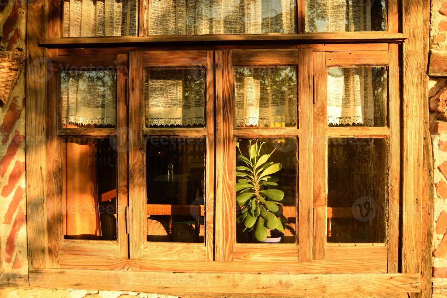 Windows of an old traditional village house with wooden frames, timbered and red bricked, in bright golden sunlight of evening hours, exterior closeup photo