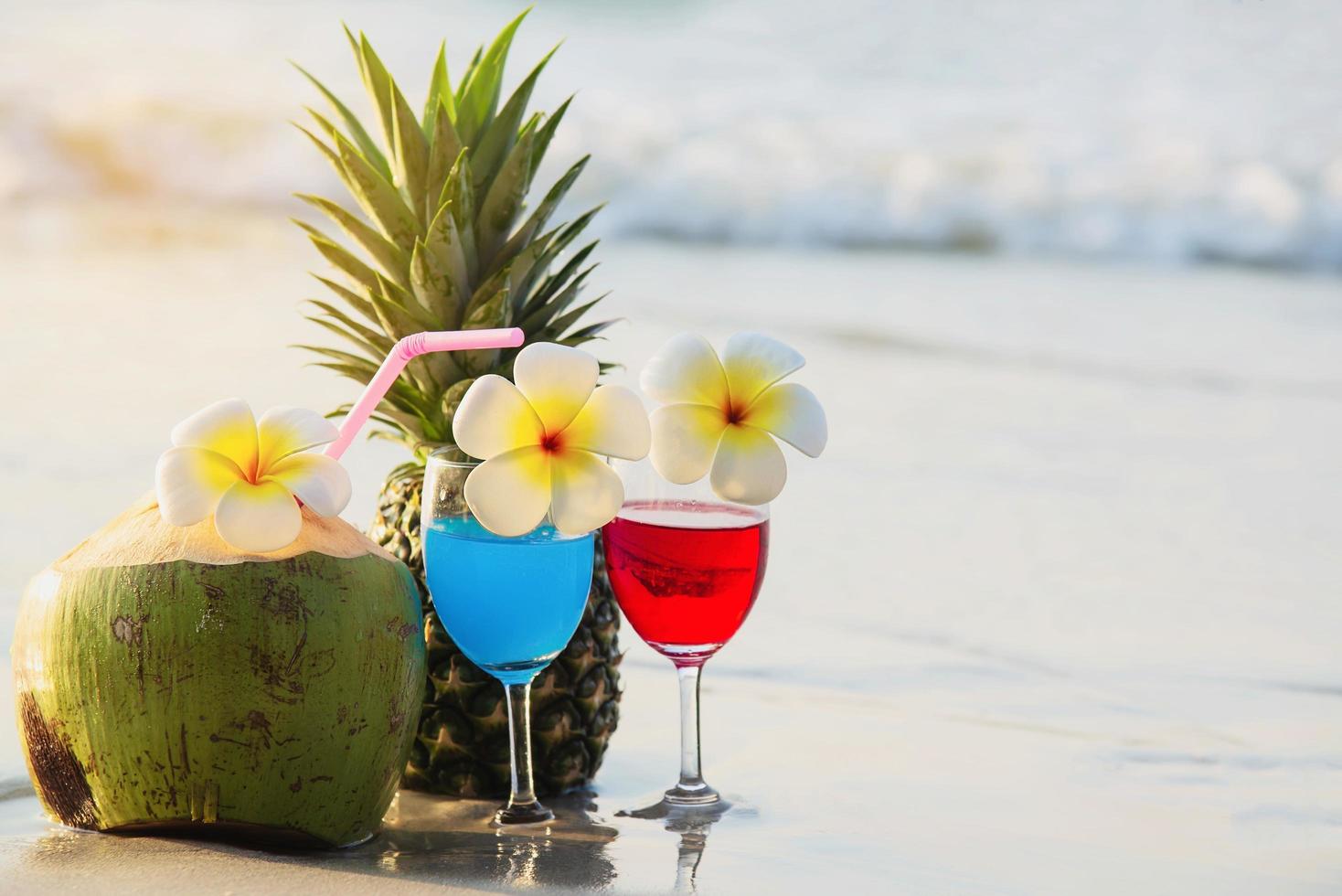 Cocktail glasses with coconut and pineapple on clean sand beach - fruit and drink on sea beach backgroudn concept photo