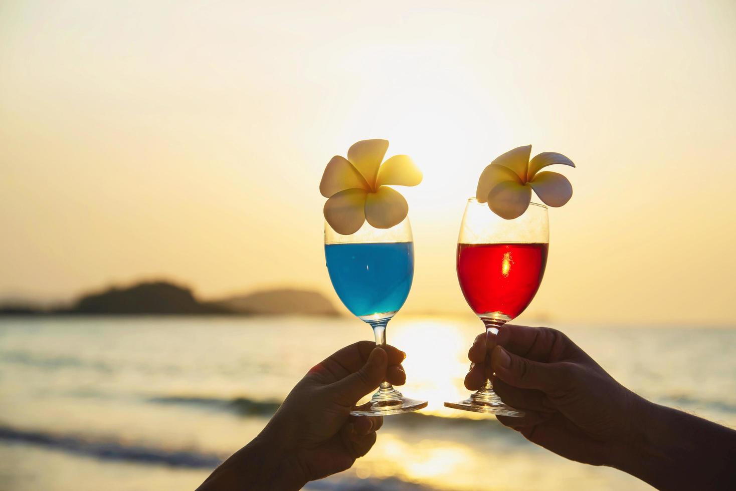Silhouette couple hand holding cocktail glass decoration with plumeria flower with beach background - happy relax celebration vacation in sea nature concept photo