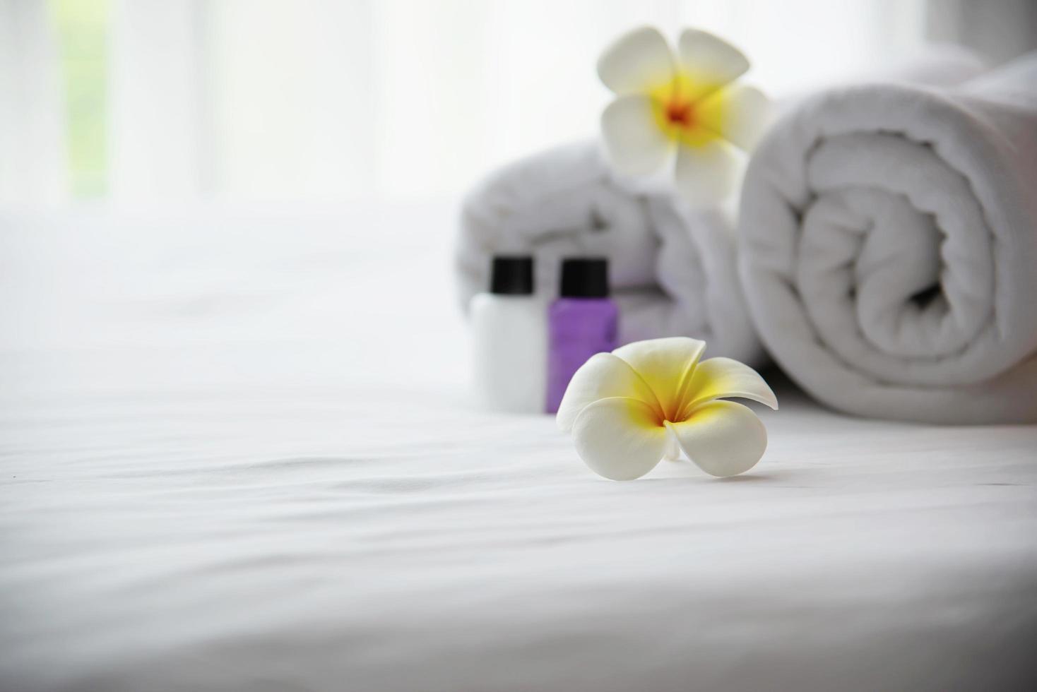 Toalla de hotel y botella de baño de champú y jabón colocadas en una cama blanca con flores de plumeria decoradas - vacaciones relajantes en el concepto de complejo hotelero foto
