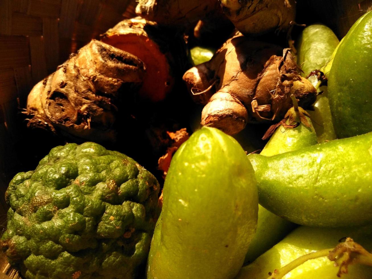 a variety of spices for cooking served in a woven bamboo container such as turmeric, ginger, bilimbi and lime. photo