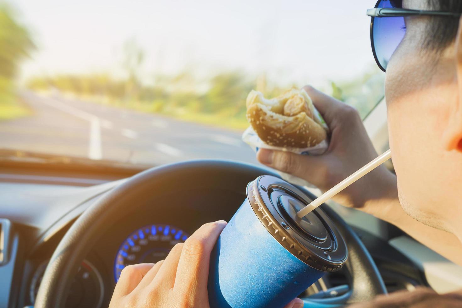 el hombre está comiendo peligrosamente un perro caliente y una bebida fría mientras conduce un automóvil foto