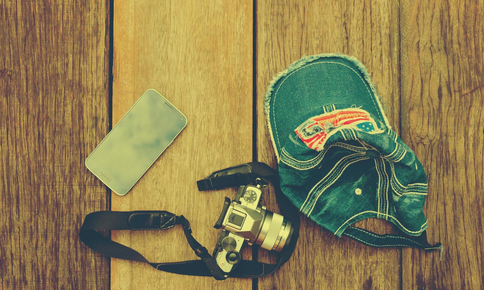 phone, camera, cap on wooden table with copyspace photo