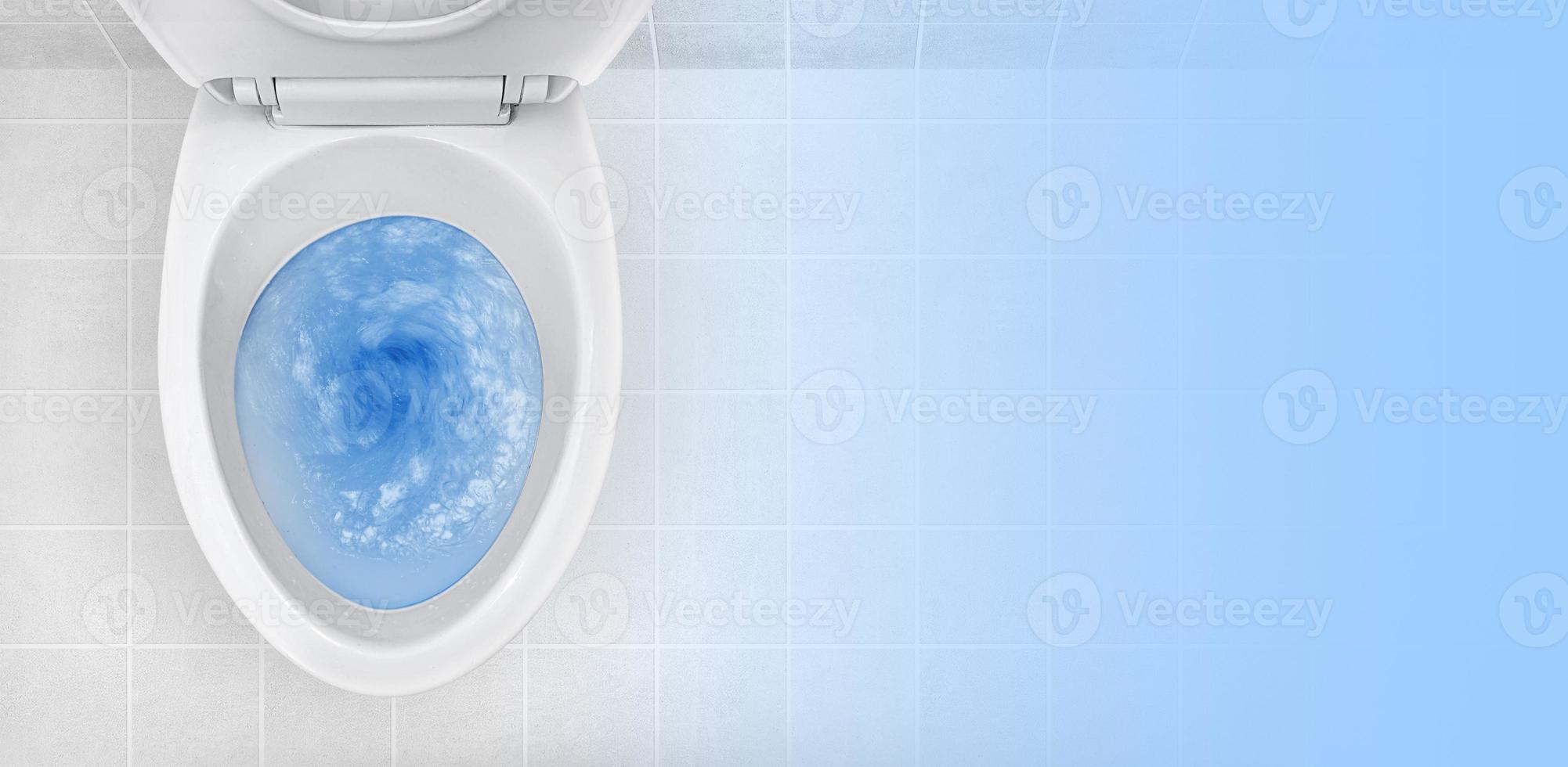 Top view of toilet bowl, blue detergent flushing in it photo