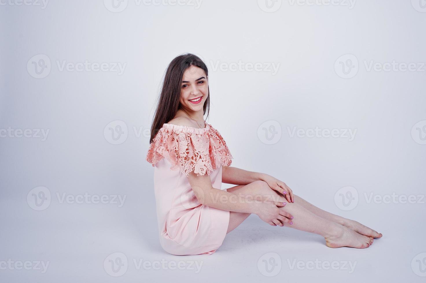 Portrait of a fashionable woman in pink dress sitting and posing on the floor in the studio. photo
