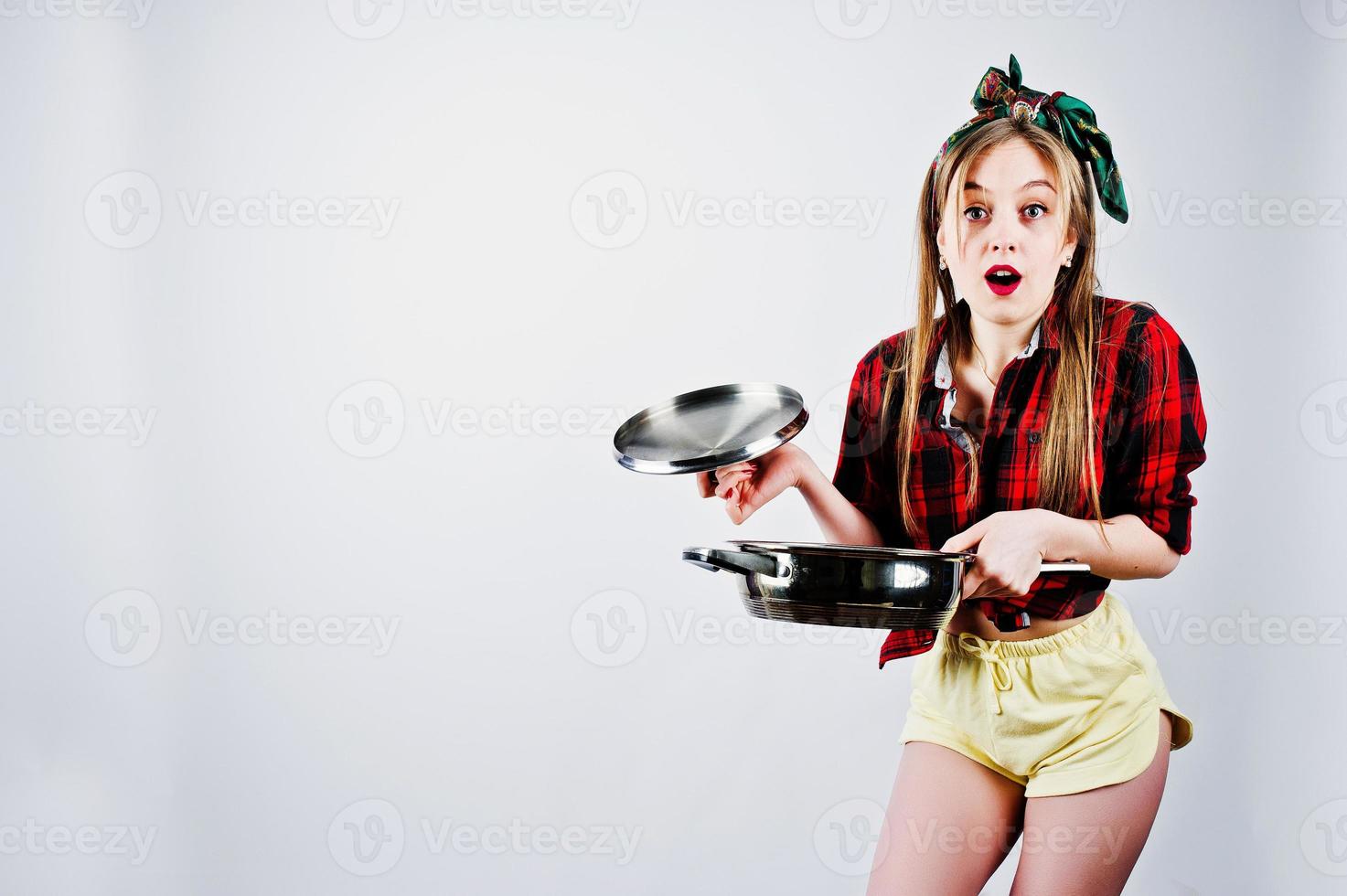 Young funny housewife in checkered shirt and yellow shorts pin up style with frying pan isolated on white background. photo