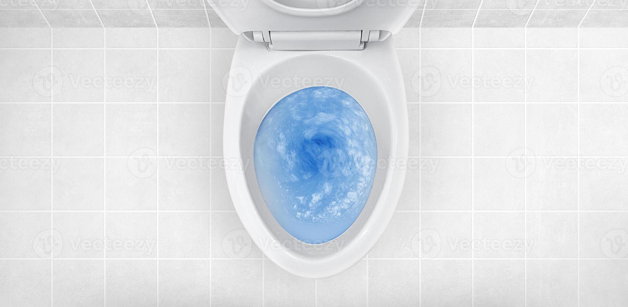 Top view of toilet bowl, blue detergent flushing in it photo