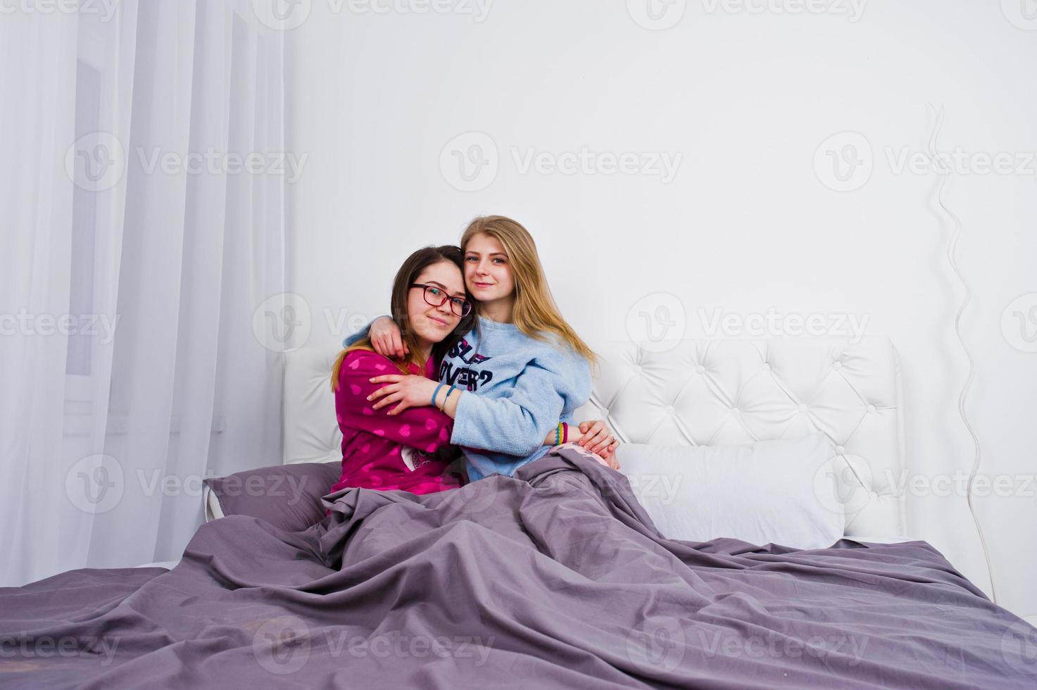 Two friends girls in pajamas having fun on bed at room. photo
