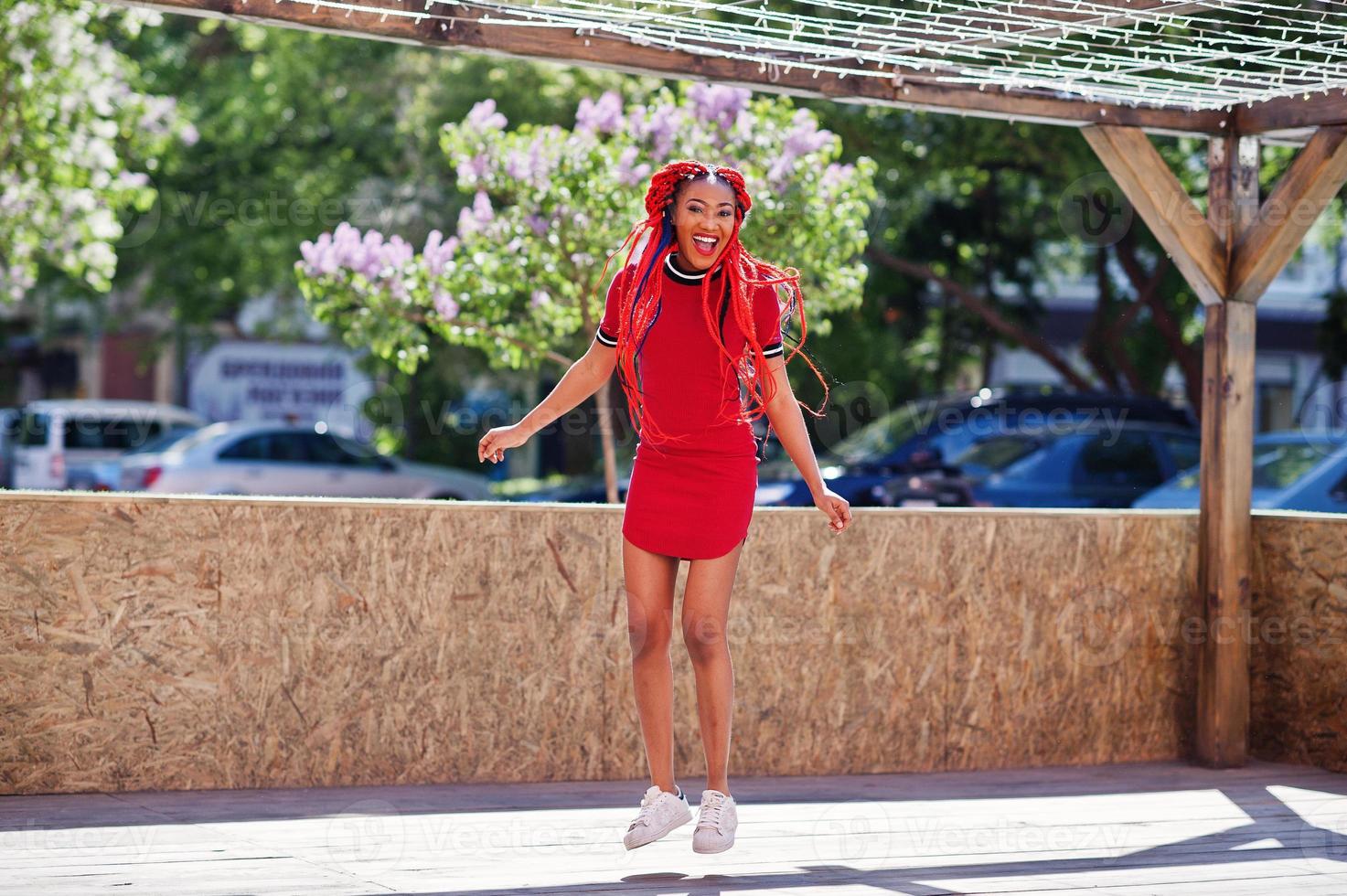 linda y delgada chica afroamericana vestida de rojo con rastas en movimiento divirtiéndose en la calle. elegante modelo negro. foto