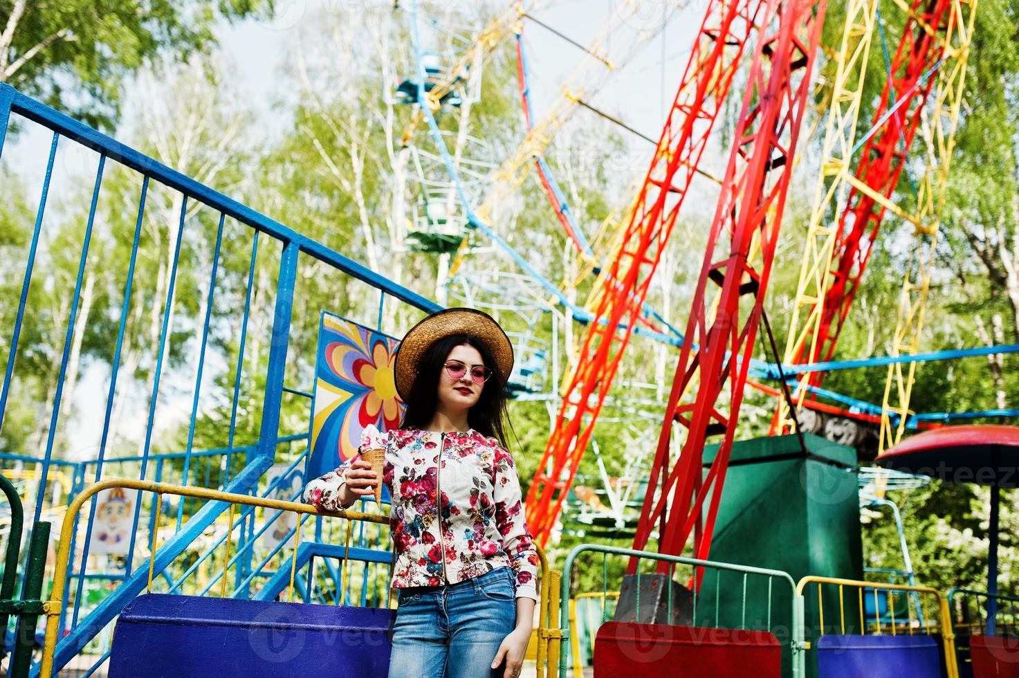 Portrait of brunette girl in pink glasses and hat with ice cream at amusement park. photo