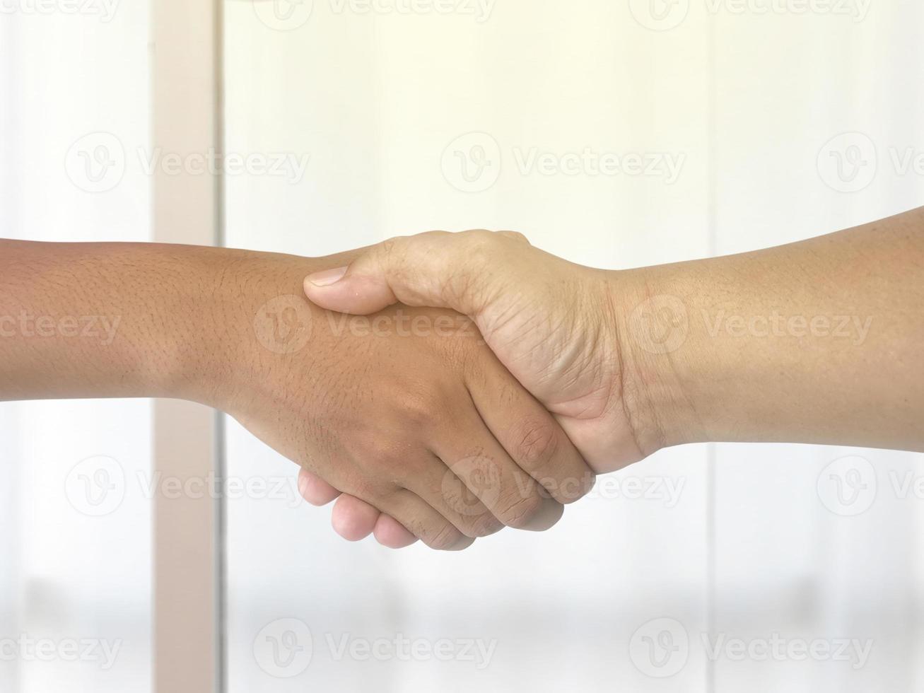 Unknown businesspeople are shaking their hands after signing a contract, while standing together in a sunny modern office, close-up. Business communication concept photo