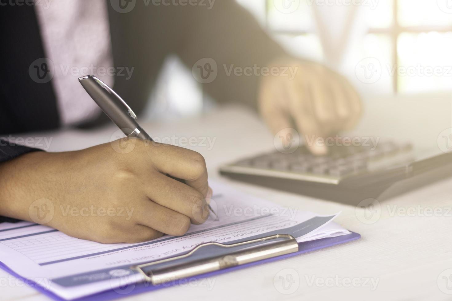 las manos de la mujer firman el formulario de reclamo de salud y la calculadora en la oficina, clínica, hospital foto