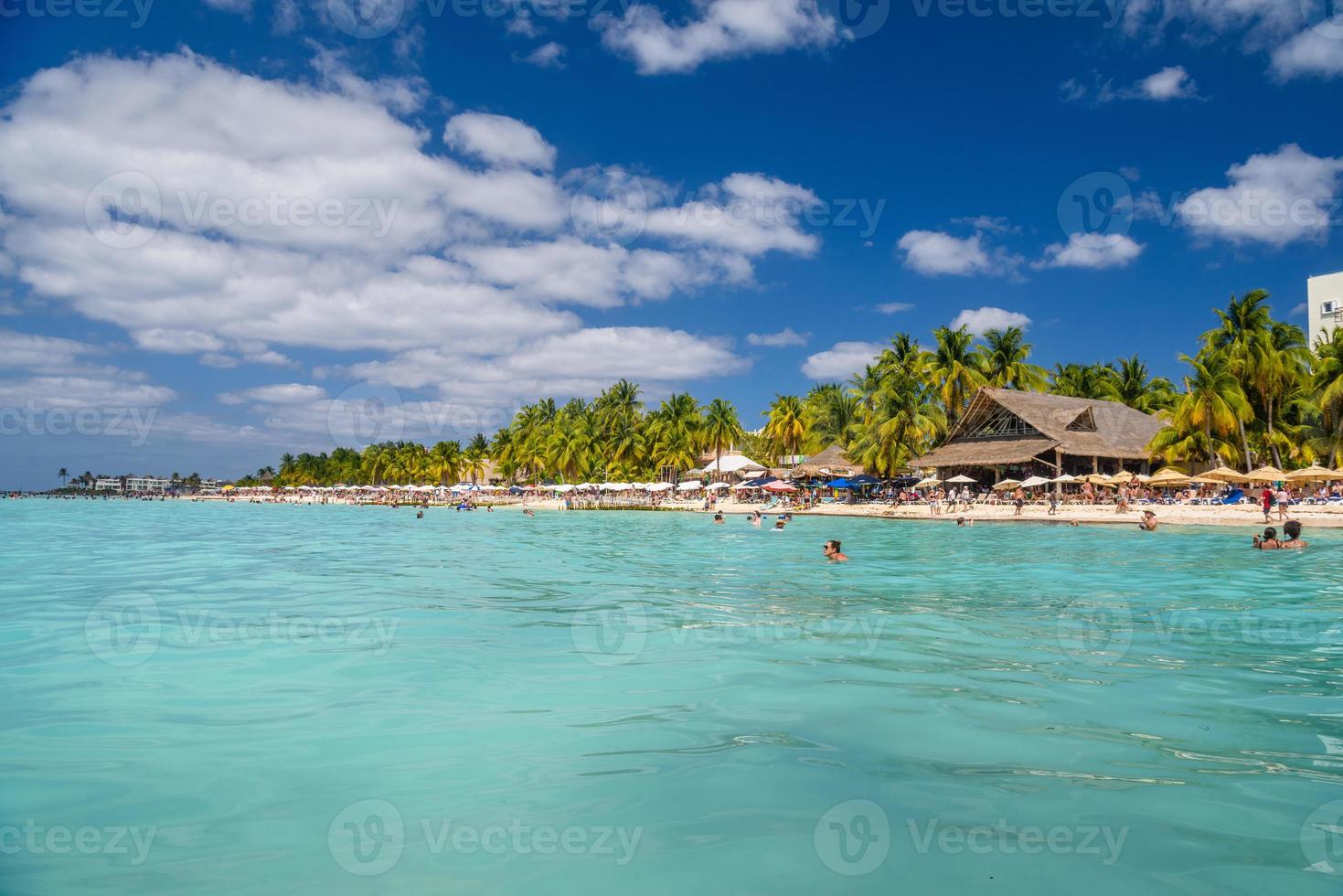 People swimming near white sand beach with umbrellas, bungalow bar and cocos palms, turquoise caribbean sea, Isla Mujeres island, Caribbean Sea, Cancun, Yucatan, Mexico photo