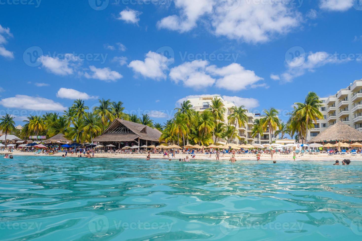 People swimming near white sand beach with umbrellas, bungalow bar and cocos palms, turquoise caribbean sea, Isla Mujeres island, Caribbean Sea, Cancun, Yucatan, Mexico photo