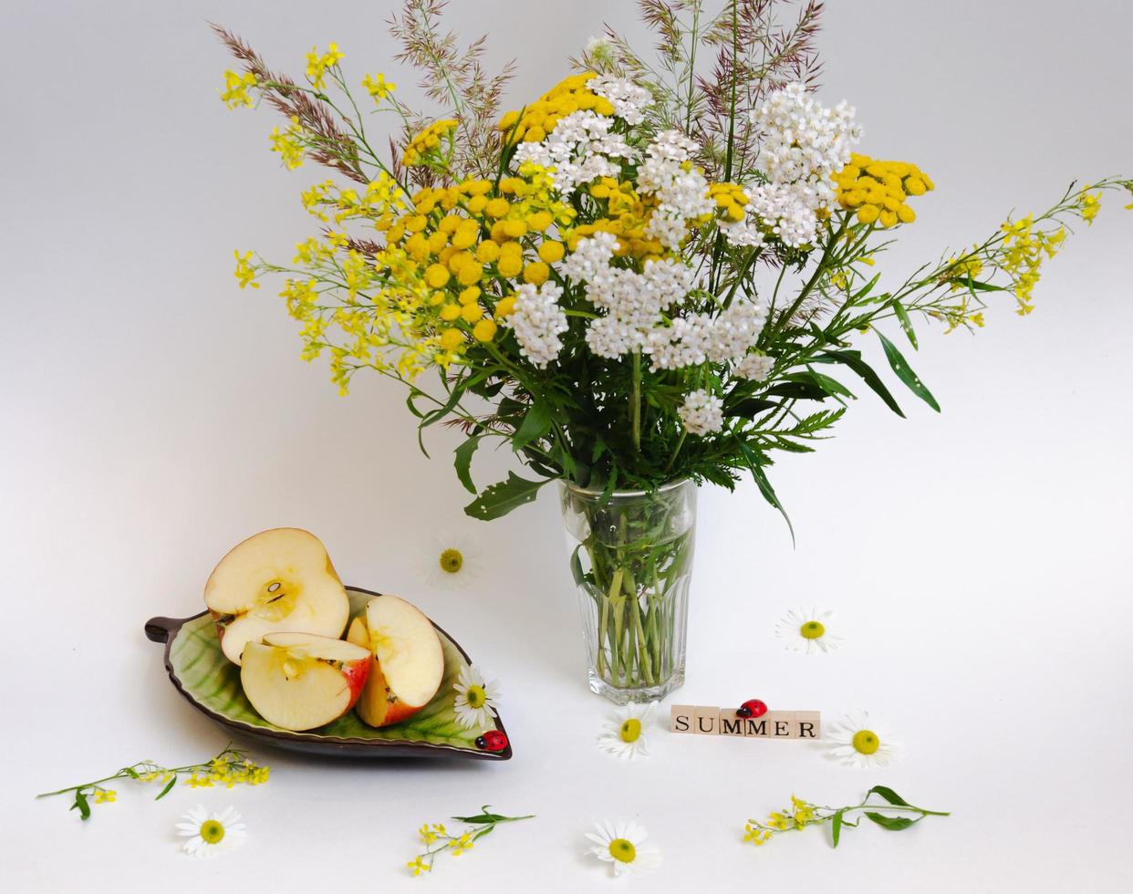 still life of wildflowers and an apple on a saucer, all on a light background photo