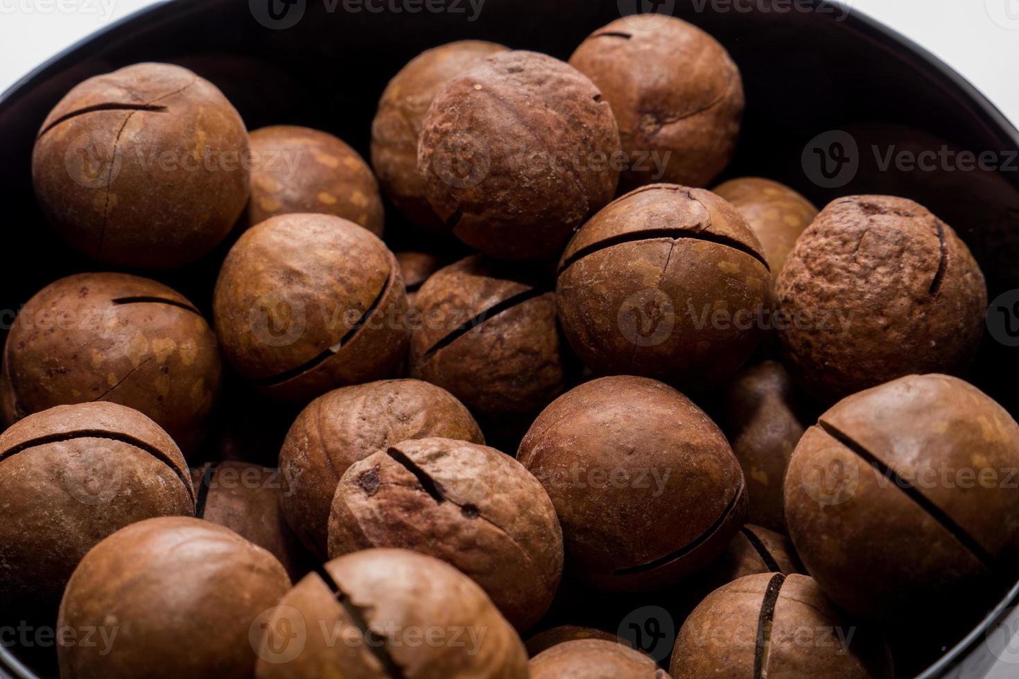 Whole macadamia nuts in black plate. Healthy vegetarian snack. Close-up photo. Vegetable diet. photo