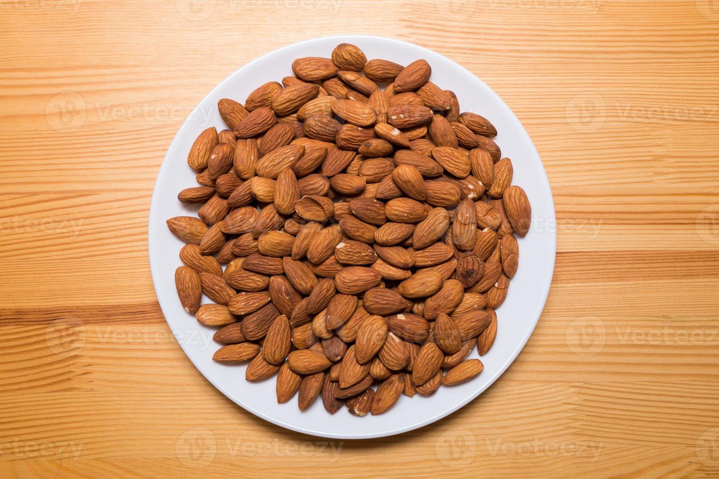 nueces enteras de almendras en un plato blanco sobre el fondo de madera. merienda vegetariana saludable. cerca de la foto. foto