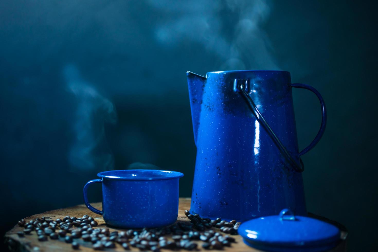 taza de café esmaltada con humo. juego de café con olla y granos de café en el viejo piso de madera foto