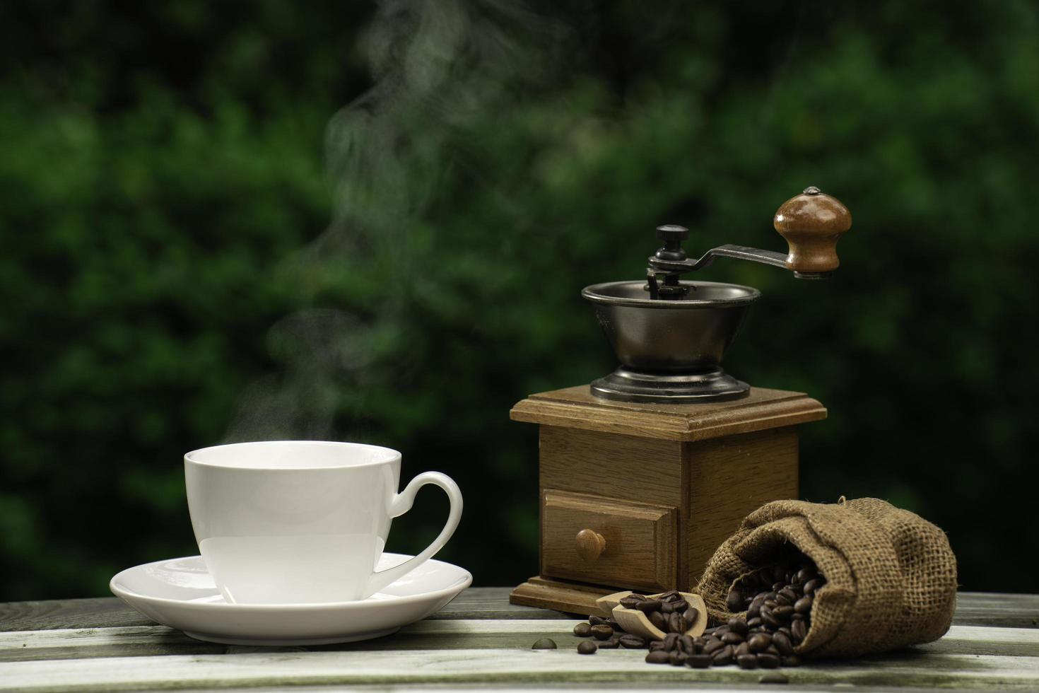 taza de café con molinillo, granos de café oscuros en el viejo piso de madera, cerca de semillas de café en un fondo natural. foto
