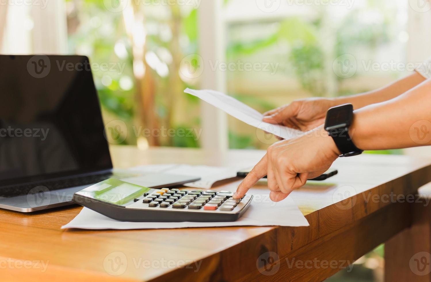 Businessman hand on calculator to calculate financial report and laptop computer on table. photo