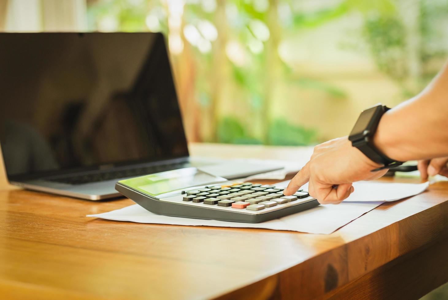 Businessman hand on calculator to calculate financial report and laptop computer on table. photo