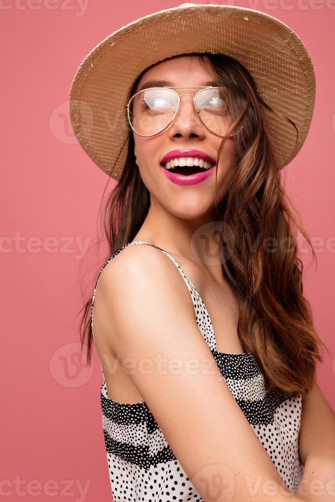 Inspired european female model looking aside with happy smile and true emotions in studio and laughing. Winsome brunette girl in cute dress posing on pink background. photo