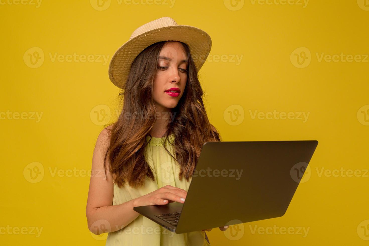 Close-up portrait of european stylish girl wearing hat with long wavy hair using laptop over isolated background photo
