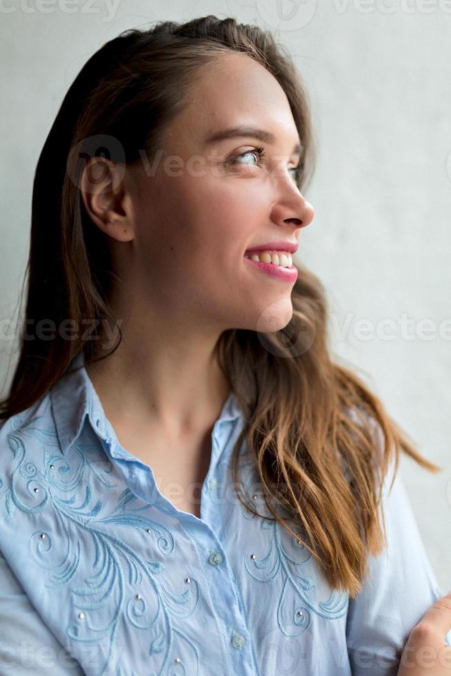 feliz chica excitada con cabello castaño y labios rosados está mirando hacia arriba con una sonrisa maravillosa cerca de la ventana en el día del sol. señora bastante adorable descansando en casa foto