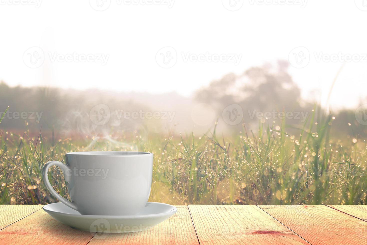 Hot coffee on Wooden table and grass field at morning photo