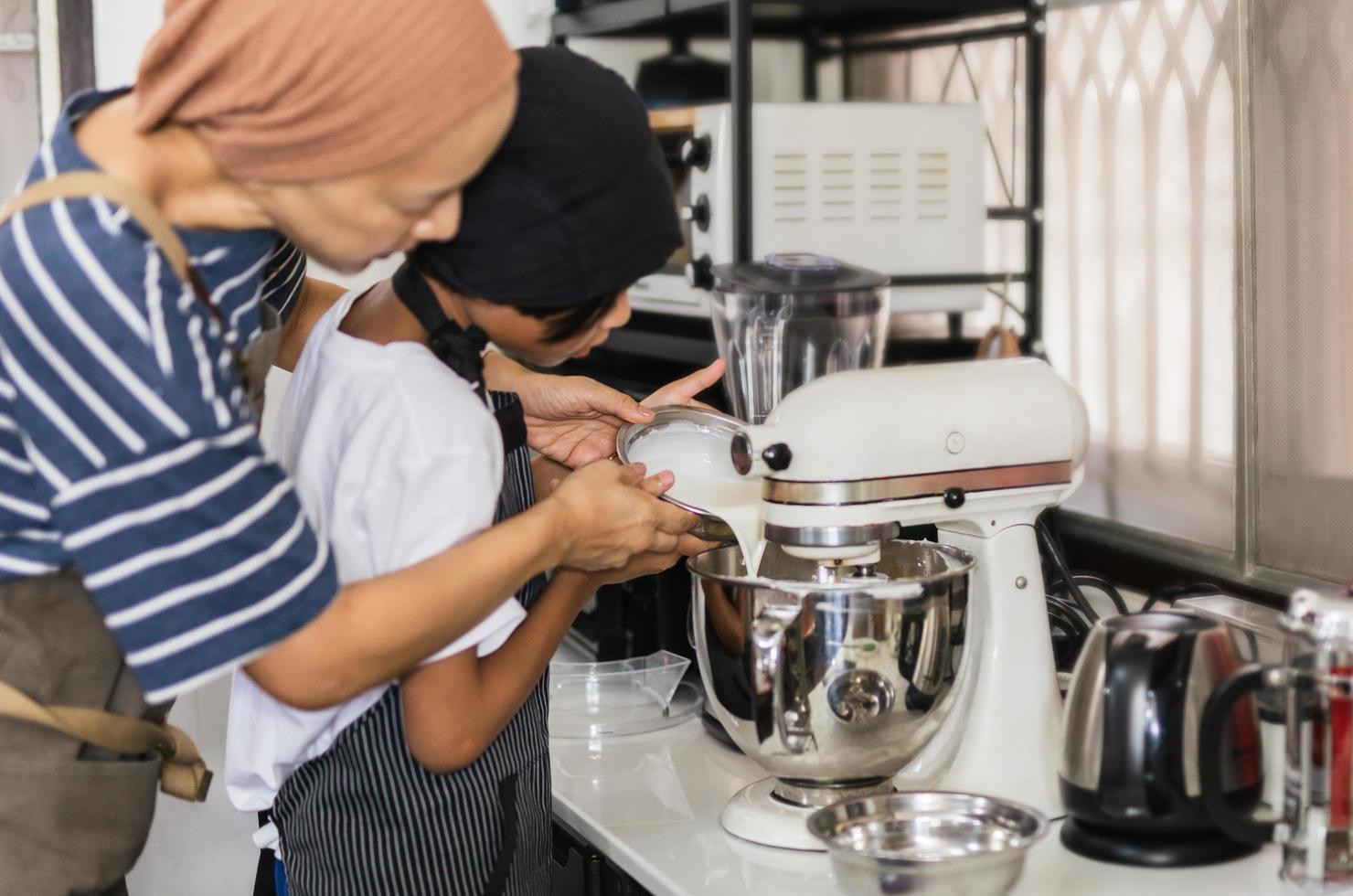 Mother teaching her son baking cake  by pouring milk into a mixing bowl. photo