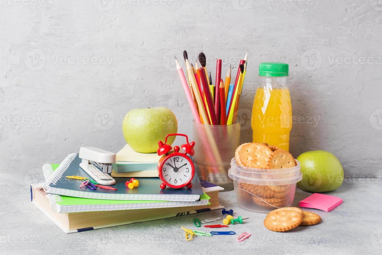 útiles escolares y galletas de desayuno, jugo de naranja y manzana fresca en la mesa gris con espacio para copiar. escuela de concepto. foto