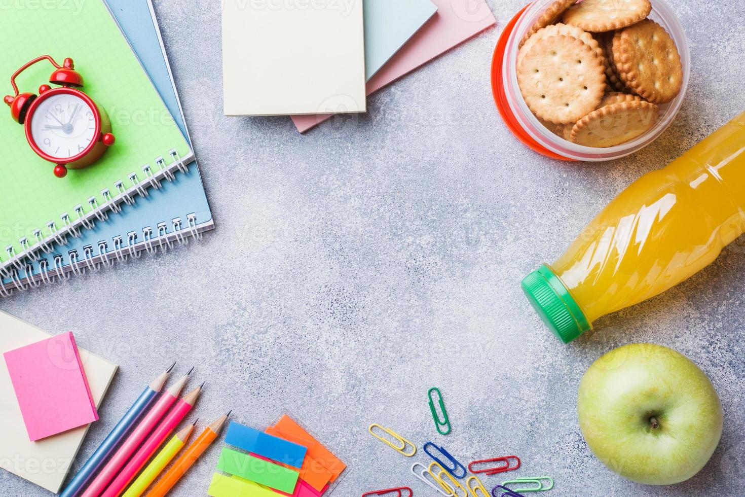 útiles escolares y galletas de desayuno, jugo de naranja y manzana fresca en la mesa gris con espacio para copiar. escuela de concepto. foto