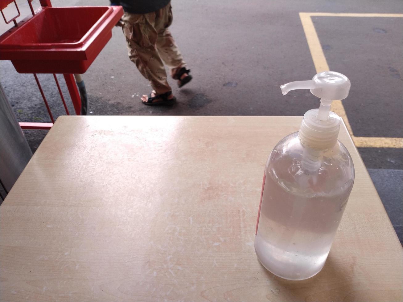 Hand sanitizer bottle on wooden table with a person walking away. Coronavirus concept photo