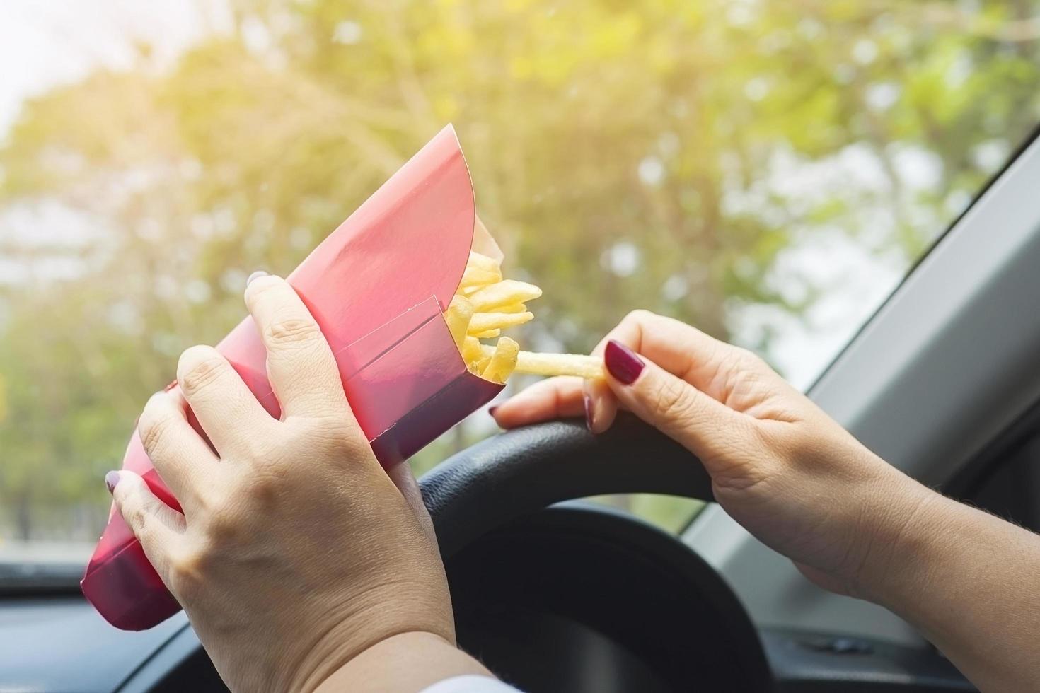 Lady eating french fries white driving car dangerously photo