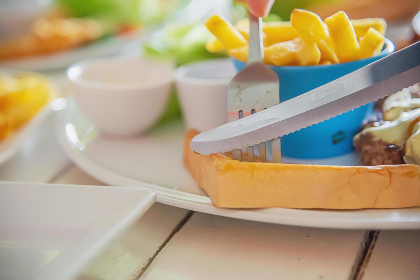 el primer plano de la gente come bistec con salchichas, patatas fritas y plato de ensalada - gente con concepto de comida rápida foto