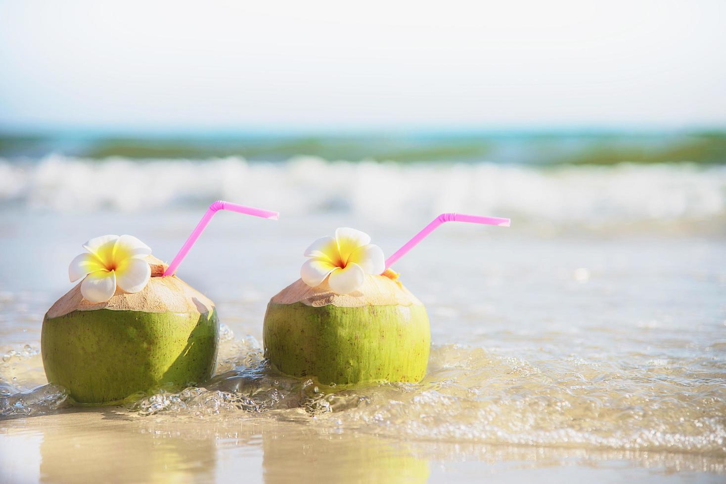 coco fresco con flor de plumeria decorada en una playa de arena limpia con fondo de olas marinas - fruta fresca con concepto de fondo de vacaciones de sol de arena marina foto