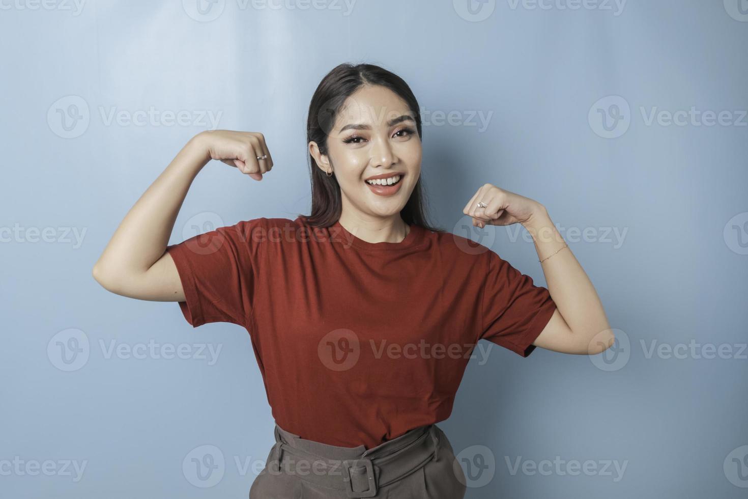 mujer asiática emocionada con una camiseta roja que muestra un gesto fuerte levantando los brazos y los músculos sonriendo con orgullo foto